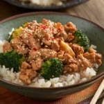 Ground chicken and broccoli stir-fry served in a bowl, with vibrant green broccoli and golden-brown chicken, garnished with sesame seeds and a drizzle of sauce.